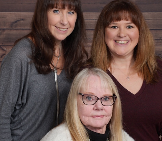 Three women standing next to each other in front of a wooden wall.